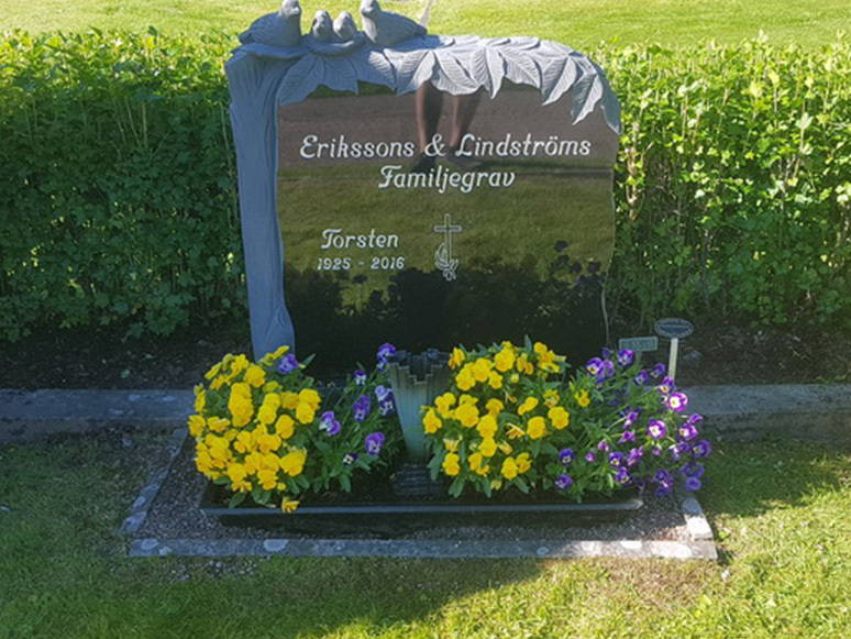 E066 i svart granit monterad på befintlig gravram. Text och dekor är försänkt målad antikvit.