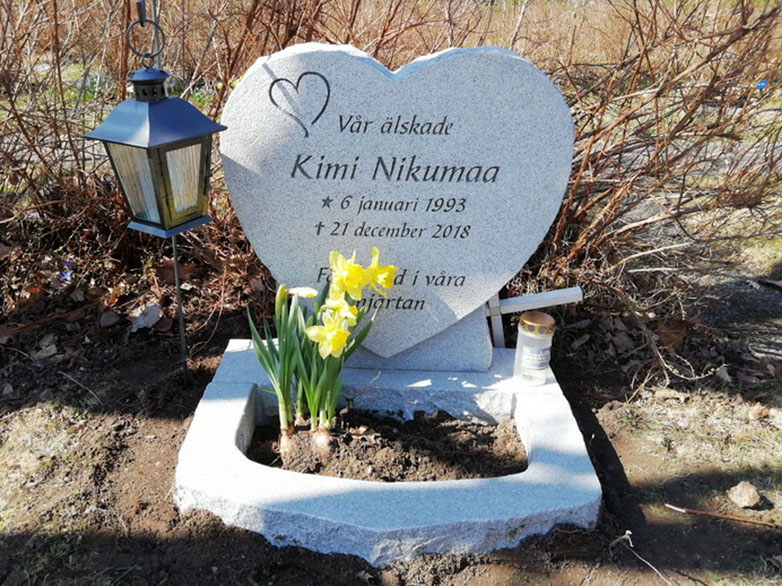 E019 i ljusgrå granit med finhuggen framsida och råarbetade sidytor. Gravyren är djupblästrad och lackad. Blomlist i oregelbunden form monterad framför sockeln.