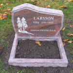 E054 in red-flamed granite, polished with roughly finished edge detail and side surfaces. Matching flower border and recessed, painted antique white text and decoration.
