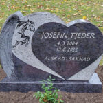 E070 i indisk blågrå granit med skulpterade vingar på sidan. Personligt dekormotiv i försänkt svart bearbetning, text försänkt silvermålad.