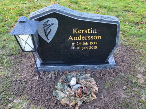 E054 in black granite, polished with a roughly finished edge detail and side surfaces. Raised decoration and recessed gilded text.