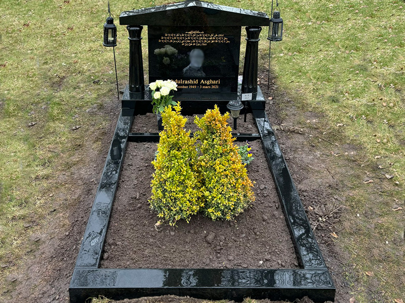 E053 i svart polerad granit. Extra djup och hög sockel, gravram med blomlist, fotoblästring samt gravyr med tecken utöver latinska alfabetet.