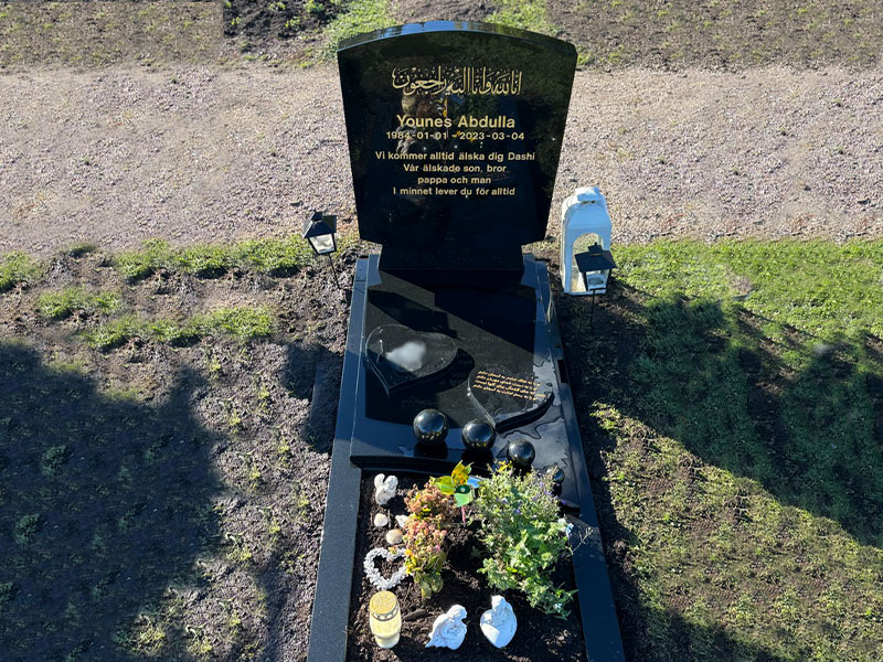 E077 i svart polerad granit, anpassade mått. Gravramsset 4, specialdesignade hjärtan, fotoblästring, tecken utöver latinska alfabetet, försänkt förgylld gravyr.