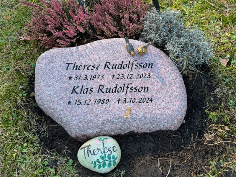 E048 i flammad indisk röd granit. Gravyren är försänkt svartmålad, bronssparvar på toppen.