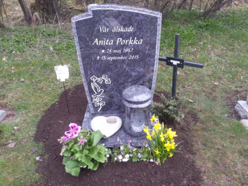 E006 i polerad indisk blågrå granit med råarbetat kantslag. Extra djup sockel och lykta, gravyren försänkt målad antikvit.