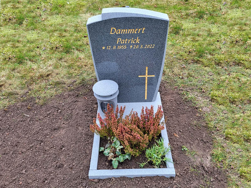 E006 i mörkgrå granit, polerad med mattslipade detaljer. Mattslipad blomlist och granitlykta samt försänkt förgylld gravyr.