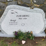 EN085 i finhuggen grå Kuru, råarbetat kantslag och sidor. Försänkt svartmålad gravyr, bronssparvar på toppen.