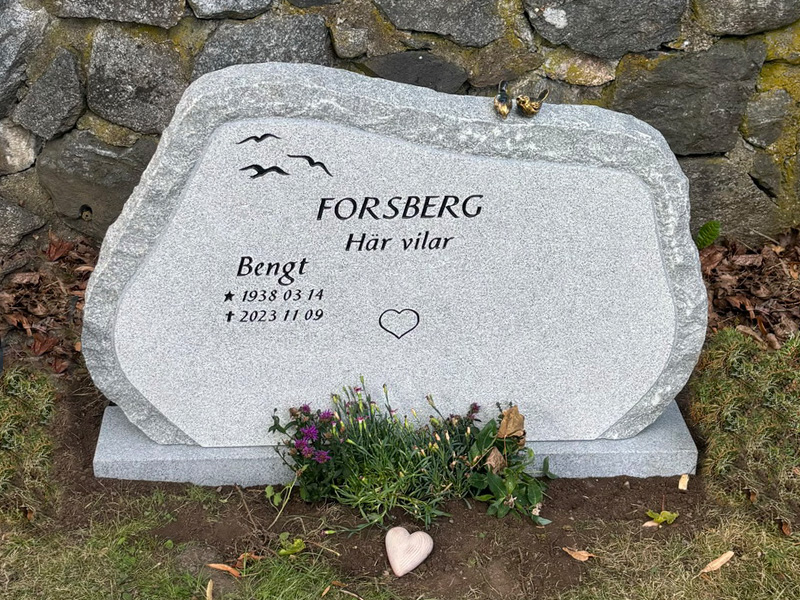 EN085 i finhuggen grå Kuru, råarbetat kantslag och sidor. Försänkt svartmålad gravyr, bronssparvar på toppen.