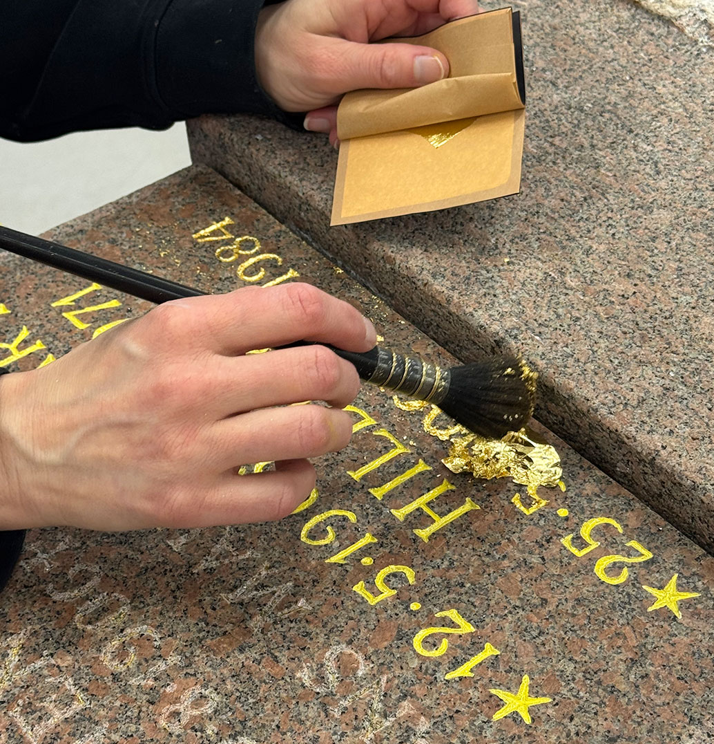 En person förgyller text på en gravsten. 